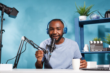 African american blogger in headphones connecting with subscribers online and looking at camera. Streamer wearing headset speaking in microphone and drinking coffee while filming video