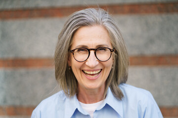 A woman with glasses is smiling and wearing a blue shirt. She looks happy and content. Concept of warmth and positivity