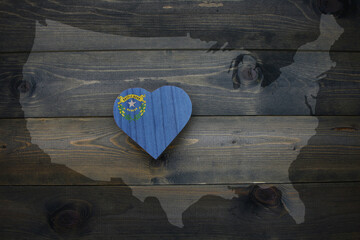 wooden heart with national flag of nevada state near united states of america map on the wooden background.