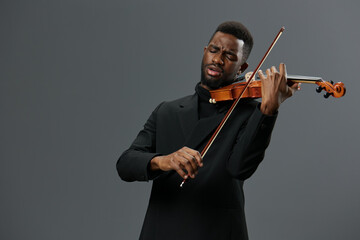 African American man in a black suit playing the violin on a gray background in a captivating...