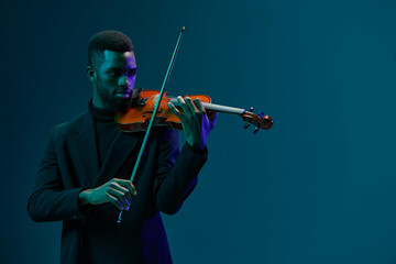 Talented African American male musician playing violin passionately on a dark blue background,...