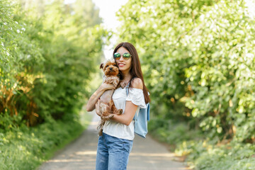 A charming girl is walking outdoor on the grass, smiling and hugging her dog. A girl and her pet are relaxing in the fresh air. Friend, friendship, care