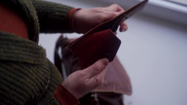 Distressed woman examines empty wallet, discovering absence of cash. Personal finance crisis, job search urgency emerge. Female checks purse, signifies poverty, need for economic assistance.
