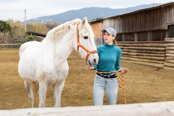 European woman horse breeder standing with white horse on paddock.