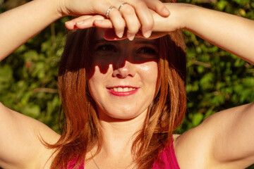 young redhead sexy woman shading her eyes with hands and arms in the sunny summer