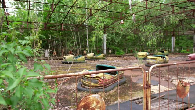 Abandoned car attraction in the city of Pripyat. The whole playground was overgrown with greenery and trees. Consequences of the Chernobyl disaster.