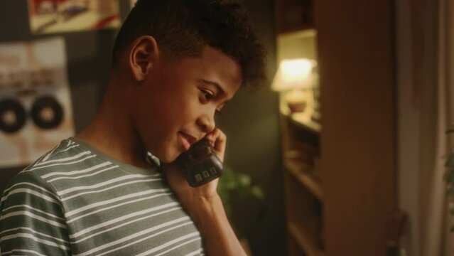 Side tilt handheld shot of Black child dialing number on vintage handset and phoning parents or friends while being alone at home with outdated interior in 90s