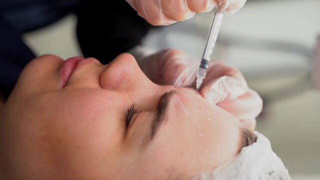 Beautician doctor makes botox injection in the forehead of young beautiful woman. Close up 4k vertical shot