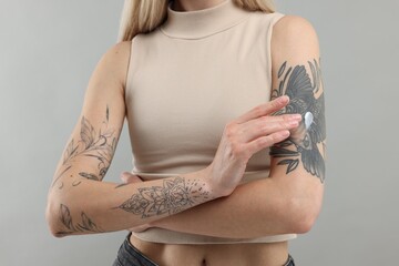 Tattooed woman applying cream onto her arm on gray background, closeup