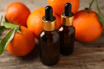 Bottles of tangerine essential oil and fresh fruits on wooden table, closeup