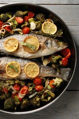 Baked fish with vegetables, rosemary and lemon on grey wooden table, top view