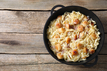Delicious scallop pasta with onion in pan on wooden table, top view. Space for text