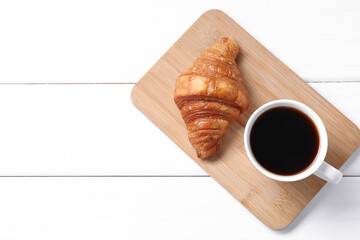 Tasty breakfast. Cup of coffee and croissant on white wooden table, top view. Space for text