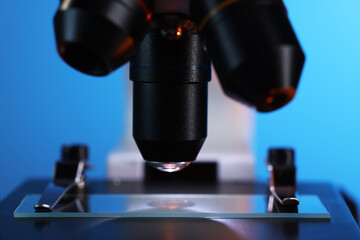 Microscope with glass slide on blue background, closeup