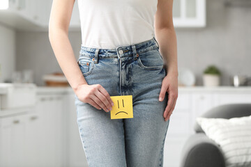 Cystitis. Woman holding sticky note with drawn sad face at home, closeup