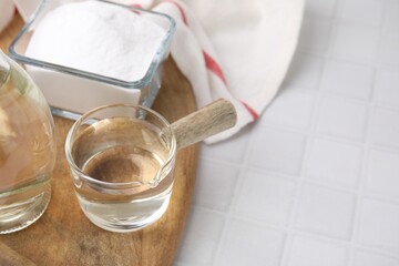 Vinegar in glass saucepan and baking soda on white tiled table, space for text