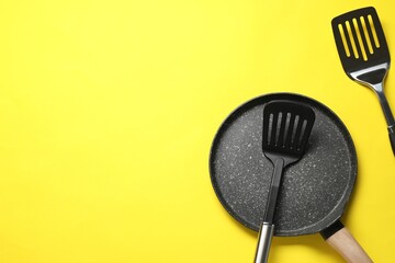 Spatulas and frying pan on yellow background, flat lay. Space for text