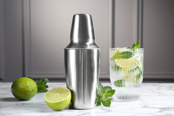 Metal cocktail shaker, delicious mojito, limes and mint on white marble table