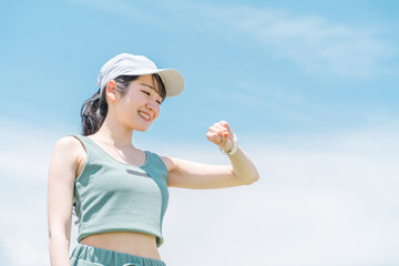 青空の下で腕時計を見ながら運動・トレーニング・ウォーキングする女性(時間・タイム・ヘルスケア)
