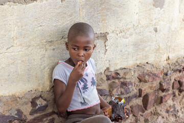 hungry small village african girl, eating snacks and biscuits, standing by the wall