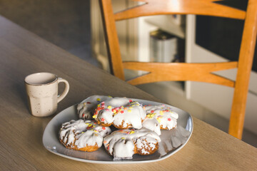 A plate of sweets with white icing, yellow red sprinkles Homemade Doughnuts, rosquillas, traditional anise donuts from Spain typically eaten in Easter, on rustic wooden table. Mediterranean sweet food