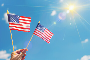 Hand holding little American flags up in the air with bright sky blue as background
