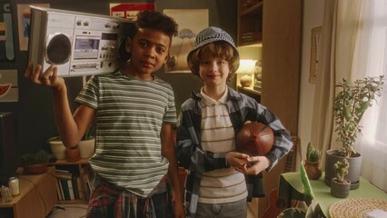 Portrait of two diverse stylish gen Y boys posing with rugby ball and boombox player while standing in cozy retro styled living room and looking at camera - Powered by Adobe