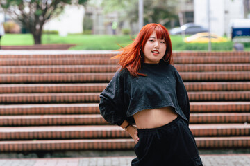 Korean woman with red hair striking a dance pose on urban steps.