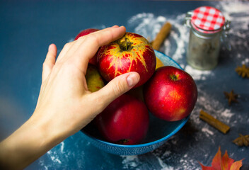 A woman's hand reaches for a ripe red apple in a bowl. Choosing fruits for making a traditional...