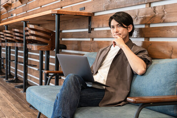 カフェ・喫茶店のソファでノートパソコンを使う若いアジア人男性
