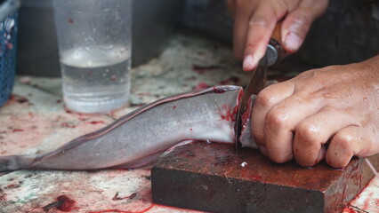 Slicing catfish using a knife on a wooden cutting board. Focus selected. Blurred background