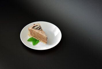 A plate with a slice of fresh cheesecake with cream and decorated with mint leaves on a black background.
