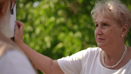 Close-up. An active couple seniors looks at a paper notice on a pole about a lost dog and talks to each other while standing in a park outdoors on a summer day