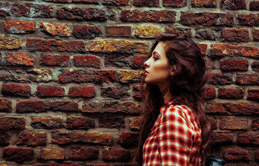Beautiful brunette make-up woman  with long hair standing on the old red brick wall building background in casual red shirt on the spring city. Closeup vintage pattern banner. Profile