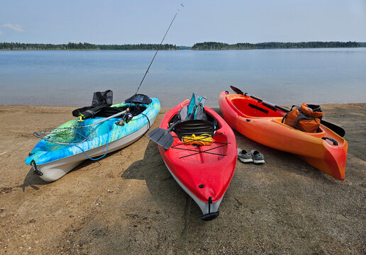 Three colorful kayaks lying on the sandy beach along the shoreline of a freshwater lake prior to launching.
