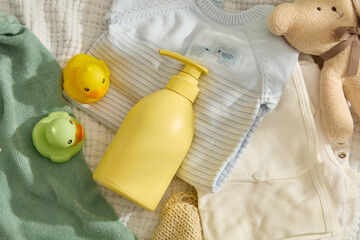 Baby clothes background photo with top view, yellow baby shower gel or shampoo bottle placed on a...