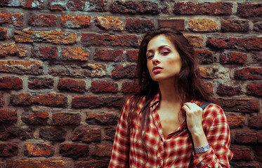 Beautiful brunette woman enjoying and standing on the old red brick wall building background in casual red shirt on the spring city. Closeup vintage banner portrait