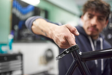 Young hispanic man assembling a bicycle in his bike shop as part of a maintenance service. Real...