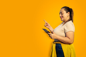 Beautiful woman in summer clothes with passport in her hand pointing at yellow background. Excited...