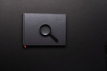 Black notebook and magnifying glass. Magnifying glass on a notebook. Search for information. Black Internet.