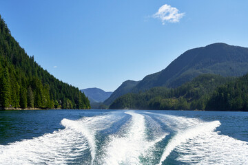 Looking out from the stern of a fast moving motor boat to it's large bright white wake which is...