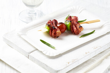 Shashlik with bacon, cherry tomato and green pepper. Bright wooden background. Close up. Copy...