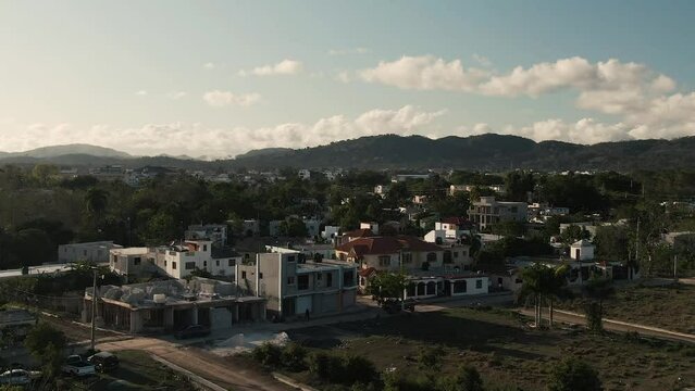 Aerial drone view of small Dominican neighborhood with mountain range at sunset 