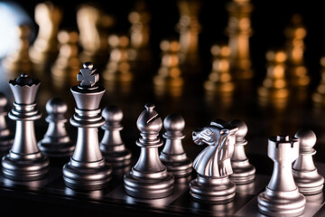 Silver chess pieces with golden figures in background.