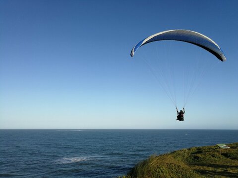 Pessoa voando de paraglider, com mar ao fundo, dia de c&eacute;u azul, sem nuvens