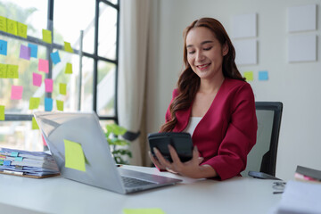 Fototapeta premium Asian businesswoman smiling at the idea of ​​working at a calculator to calculate income. on the laptop at the office.