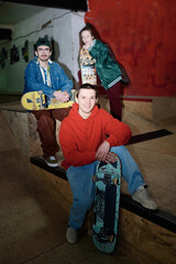 Vertical long flash shot of modern gen Z Caucasian guys and girl posing for camera with skateboards in skatepark, copy space