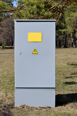 Transformer substation in the park. Grey metal cabinet against a background of pine trees. Outdoor electric switchboard or cabinet. Spring, pine branches.