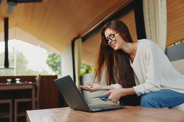 Smiling woman sitting on a sofa with a laptop, teaching online She wears glasses and looks relaxed...