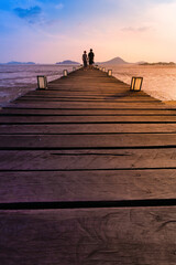 Silhouette of a couple walking on a wooden pier at sunset with a scenic view
